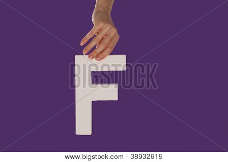 Femelle main tenant vers le haut de la lettre majuscule F isolé contre un fond violet vue
