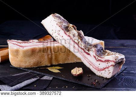 Chunks Of Salted Bacon On Dark Background. Healthy Food With Pranami And Herbs. Salted Fat, Lard, Ta