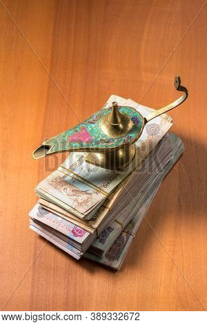 An aladdin lamp placed over pile of hundred dirham currency notes on wooden background.