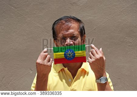 A Man And Hygienic Mask With Ethiopia Flag Pattern In His Hand And Raises It To Cover His Face On Br