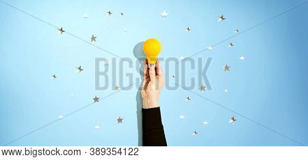 Person Holding A Yellow Light Bulb With Silver Shiny Stars