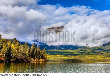 The lake is covered with light water ripples. Pyramid Lake. Mount Pyramid is covered by lush cumulus clouds. Cold sunny day in the Rocky Mountains of Canada. 