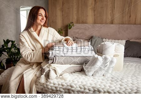 Beautiful Woman In Winter Thick Warm Robe Is Sitting And Neatly Folding Bed Linens And Bath Towels