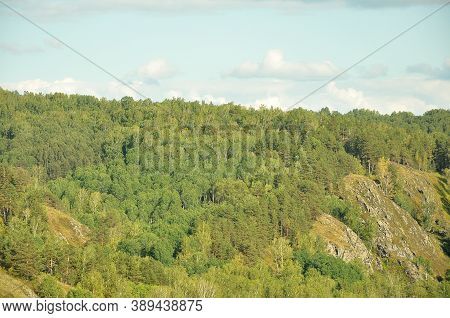 Large Mountain Range Overgrown With Dense Coniferous Forest Under A Cloudy Sky.