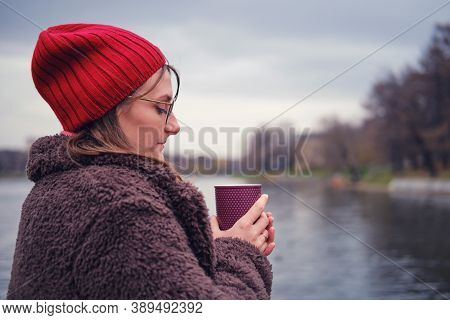 Woman Stands In A Coat With A Cup Of Coffee Near The Winter Lake