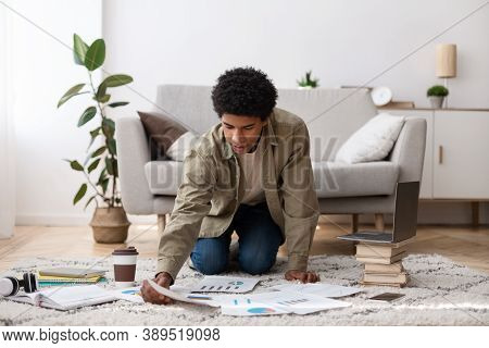 Full Length Portrait Of Black Teen Guy Arranging Materials For His Coursework Paper On Floor At Home