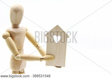 A Wooden Mannequin Or Doll Holding A Wooden House With A Heart On A White Background. Copyspace.