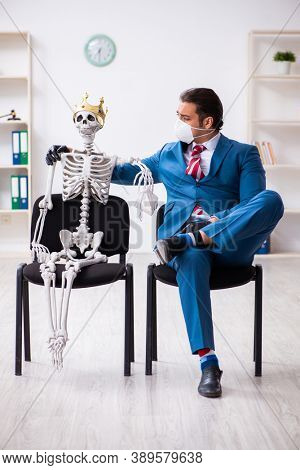 Young businessman and skeleton in the office in pandemic concept
