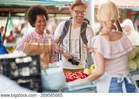 Seller woman offers fresh and organic vegetables and fruits at the green market or farmers market stall.  Young buyers choose and buy products for healthy food in grocery. 