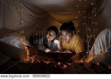 Family Concept. Elder Sister And Sister Reading Book With Flashlight Together Before Bedtime. Sister