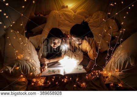 Family Concept. Elder Sister And Sister Reading Book With Flashlight Together Before Bedtime. Sister