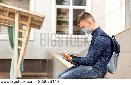 Teen Boy Sitting In The Background Of The School. He Reads Textbooks. His Face In A Medinah Face Mas