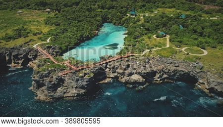 Cliff sea coastline with green landscape with limpid lake on top in aerial view. Scenic seascape admist tropic greenery nature at Weekuri lagoon, Sumba Island, Indonesia. Cinematic drone shot