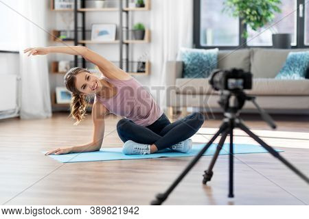 fitness, sport and video blogging concept - woman or blogger with camera streaming online yoga class at home
