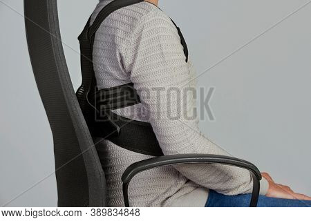 closeup of a young caucasian man wearing an upper back posture corrector as is sitting at his office chair