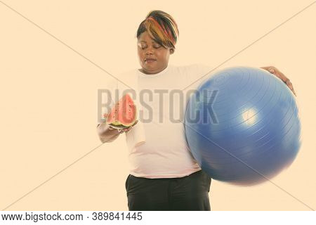 Studio Shot Of Fat Black African Woman Holding Exercise Ball And Looking At Slice Of Watermelon Read