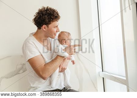 Happy young father playing with his little cutr baby son while laying in bed at home, embracing