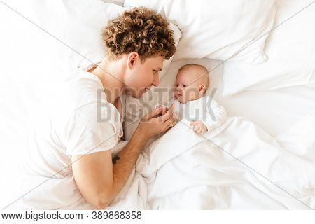 Happy young father playing with his little cutr baby son while laying in bed at home, embracing