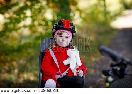 Little Toddler Girl With Security Helmet On Head Sitting In Bike Seat Of Her Mother Or Father Bicycl
