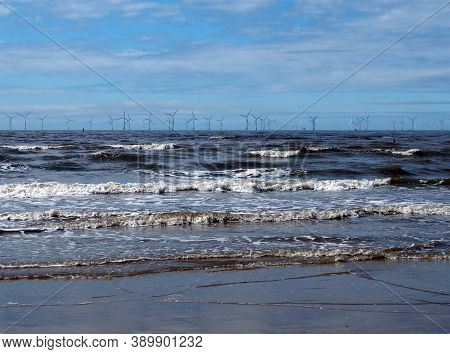 The Beach At Blundell Flats In Southport With Waves Braking On The Beach And The Wind Turbines At Bu