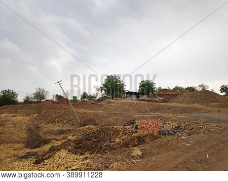 Broken Electricity Pole Beside Road In Indian Rural Area With A Small House In Background On A Hill