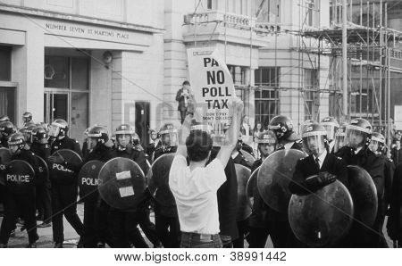 LONDON - MARCH 31: A protestor holds up a poster in front of riot police during the Poll Tax Riots on March 31, 1990 in London. The demonstration was against the unpopular Community Charge.