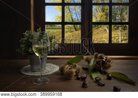 Chestnuts And A Glass Of White Wine On The Table In Front Of The Window On An Autumn Day