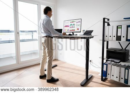 Man Working On Computer At Standing Desk In Home Office