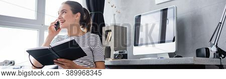 Panoramic Of Teleworker Talking On Smartphone And Holding Notebook At Home