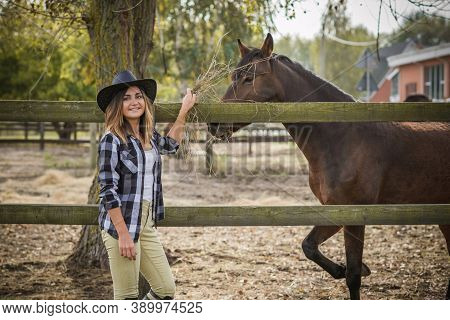 American Woman On A Horse Farm. Portrait Of Girl In Cowboy Hat With A Horses. Hippotherapy At Nature