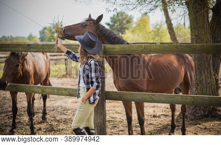 American Woman On A Horse Farm. Portrait Of Girl In Cowboy Hat With A Horses. Hippotherapy At Nature