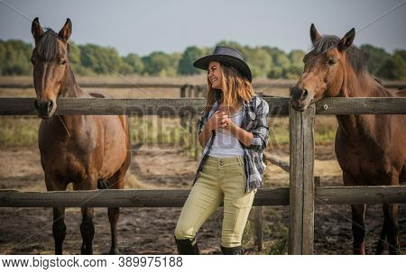 American Woman On A Horse Farm. Portrait Of Girl In Cowboy Hat With A Horses. Hippotherapy At Nature
