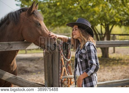 American Woman On A Horse Farm. Portrait Of Girl In Cowboy Hat With A Horses. Hippotherapy At Nature