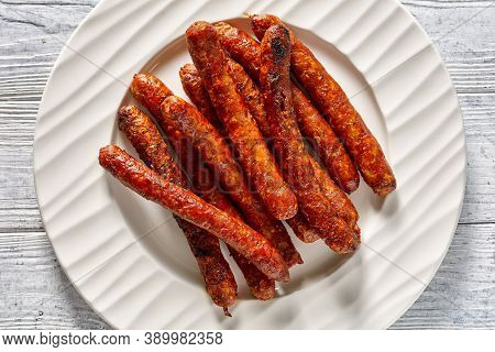 Short French Sausages Chipolata Grilled And Served On A White Plate On A White Wooden Background, To