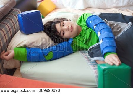 Beautiful Biracial Disabled Little Boy Lying Down On Mattress Playing With Foam Blocks While Wearing