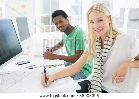 Side view portrait of an artist drawing something on paper with pen besides male colleague at the office