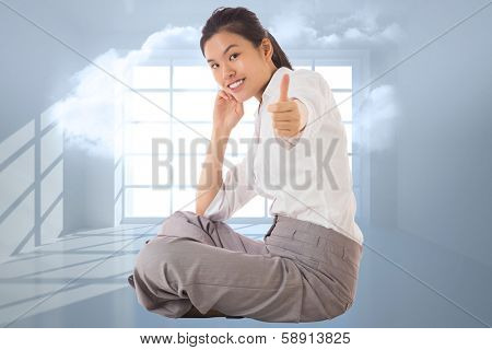 Businesswoman sitting cross legged showing thumb up against room with holographic cloud