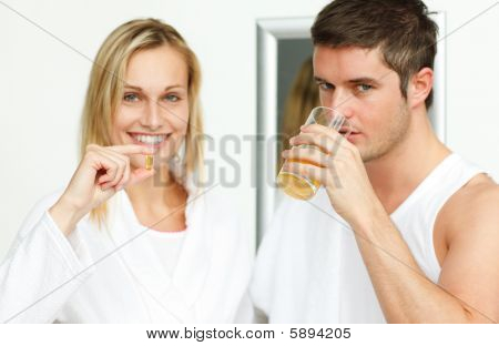 Mulher segurando pílulas e homem beber suco de laranja