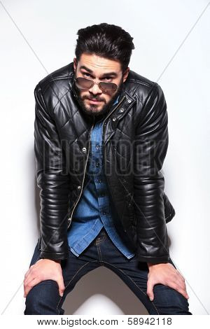 tired fashion man resting against studio wall and looks at the camera