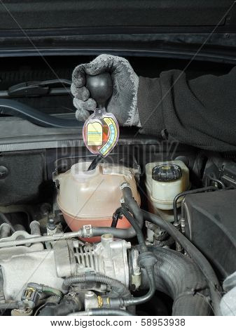 Auto mechanic performing antifreeze coolant freeze-up protection test using a tester