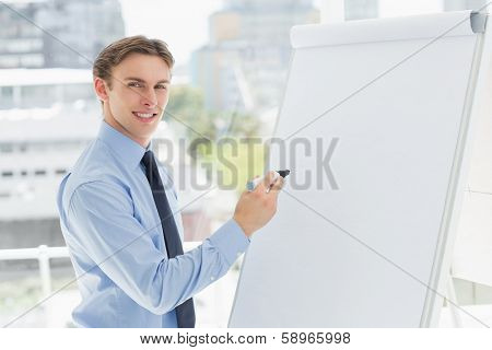Young smiling businessman writing on whiteboard with marker in the office
