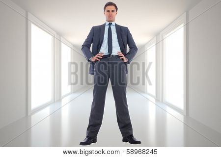 Serious businessman with hands on hips against digitally generated room
