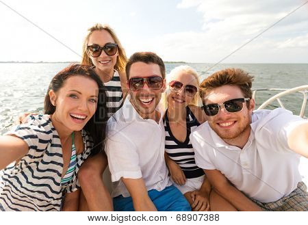 vacation, travel, sea, friendship and people concept - smiling friends sitting on yacht deck and making selfie