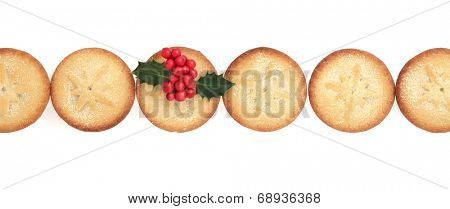 Christmas mince pie cakes in a line with holly over white background.
