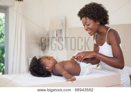 Happy mother with baby girl on changing table at home in the bedroom