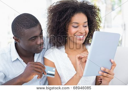Attractive couple using tablet together on sofa to shop online at home in the living room
