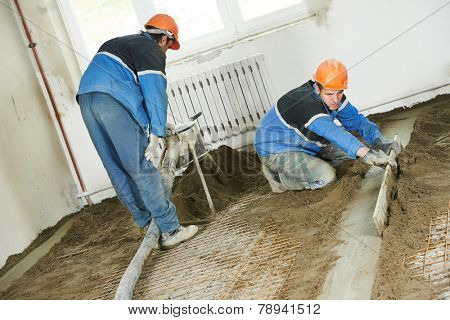 Plasterer workers at indoor concrete cement floor topping with float