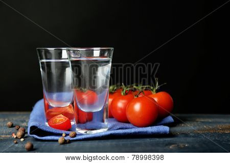 Glasses of ouzo and tomatoes on wooden table, on grey background