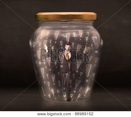 Business man trapped in jar with exclamation marks concept on bakcground