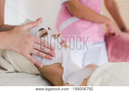 Female cosmetologist making cosmetic facial mask to the female client at the cosmetology centre.